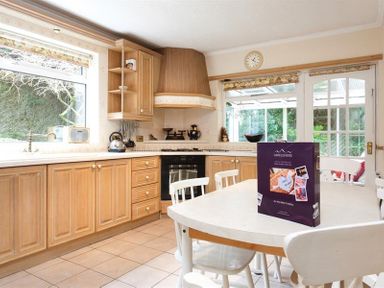 A kitchen with wooden cabinets a white table with chairs and a purple box on the table at Nutwood in Lakeside