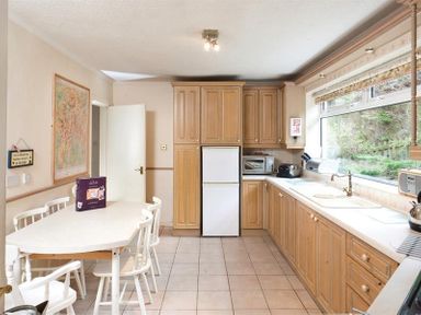 A kitchen with wooden cabinets white appliances tiled floor a white dining table with chairs and a large window at Nutwood in Lakeside