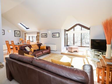 A living room with leather sofas cushions a wooden dining table and large windows at Spring Cottage in Ambleside