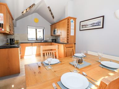 A kitchen and dining area with wooden cabinets and a table set with plates and glasses at Spring Cottage in Ambleside