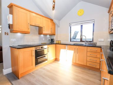 A kitchen with wooden cabinets black countertops an oven a sink a window and a yellow clock at Spring Cottage in Ambleside