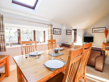 A dining area with a wooden table set with plates and glasses and a living area with brown leather sofas and a television at Spring Cottage in Ambleside