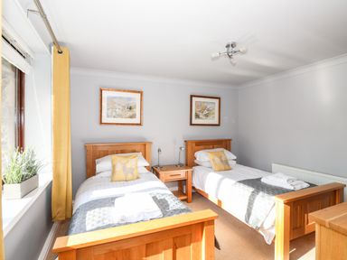 A bedroom with two single wooden beds a nightstand between them and framed pictures on the wall at Spring Cottage in Ambleside
