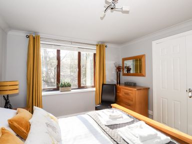 A bedroom with a bed towels dresser chair mirror and window with yellow curtains at Spring Cottage in Ambleside