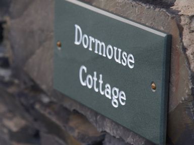 A close up of a green sign with white text mounted on a stone wall at Dormouse Cottage in Coniston