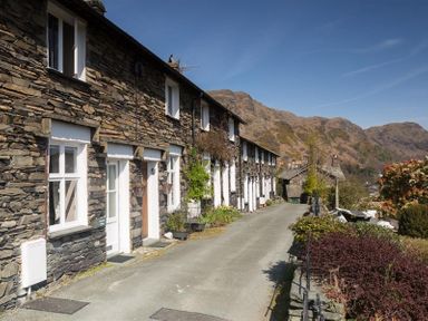 A row of stone cottages with white doors and windows along a narrow road with hills in the background at Dormouse Cottage in Coniston