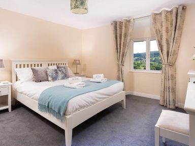 A bedroom with a bed side tables a chair a window with curtains and a view at Dormouse Cottage in Coniston