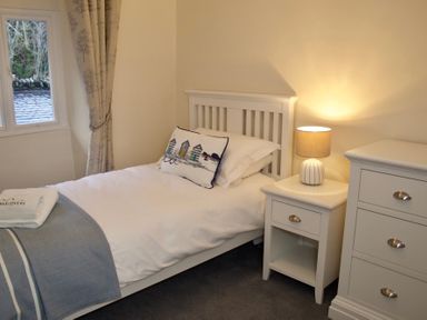 A bedroom with a single bed beside a window a nightstand with a lamp and a chest of drawers at Dormouse Cottage in Coniston