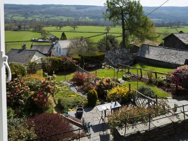 A garden with flowering shrubs a table and bench and surrounding houses overlooking fields and hills at Dormouse Cottage in Coniston