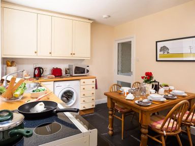 A kitchen with wooden dining table set for a meal and white cabinets with appliances at Dormouse Cottage in Coniston