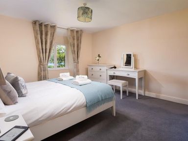 A bedroom with a bed towels on a light blue throw and a white dressing table with a stool at Dormouse Cottage in Coniston
