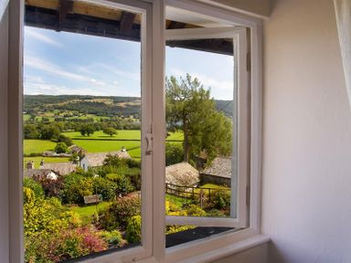 A view of green fields trees and houses seen through a window at Dormouse Cottage in Coniston