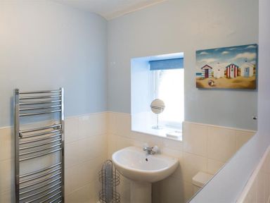 A bathroom with a pedestal sink a towel rack and a window with a small mirror and a painting on the wall at Dormouse Cottage in Coniston