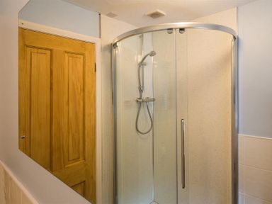 A bathroom with a glass enclosed shower and a wooden door at Dormouse Cottage in Coniston