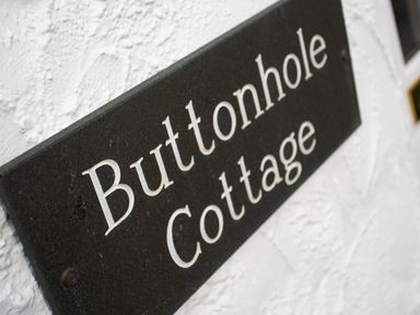 A close up of a black sign with white text mounted on a white textured wall at Buttonhole Cottage in Ambleside