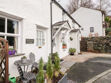Front exterior of a white cottage with small table and chairs near the door at Buttonhole Cottage in Ambleside