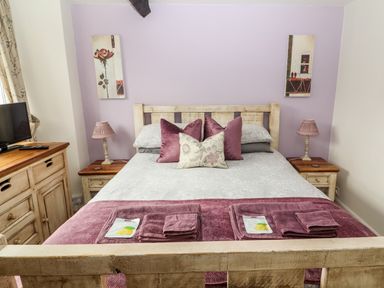 A bedroom with a bed with pillows and folded towels along with lamps on bedside tables at Buttonhole Cottage in Ambleside