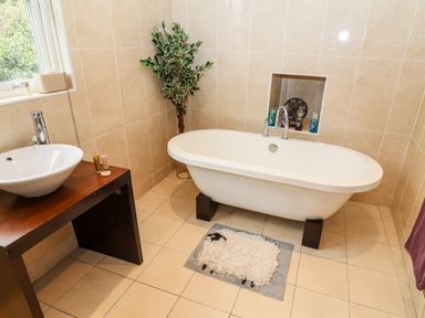 A bathroom with a freestanding bathtub a sink on a wooden counter a plant and a sheep-shaped rug at Buttonhole Cottage in Ambleside