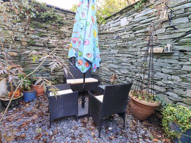 A garden with a table and chairs under an umbrella at Buttonhole Cottage in Ambleside
