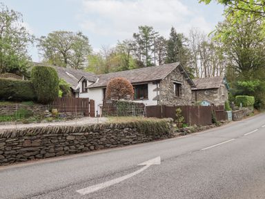 A stone and white plaster house with a wooden fence and trees along a road at Old Coach House Ambleside