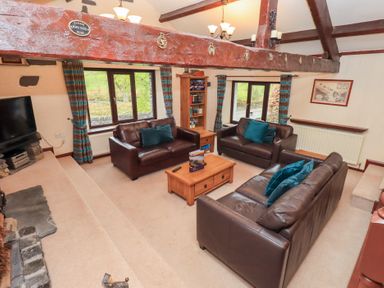 A living room with brown leather sofas a wooden coffee table a bookshelf and windows with blue striped curtains at Old Coach House Ambleside