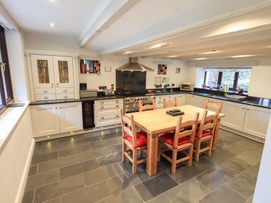 A kitchen with a wooden dining table and six chairs with red cushions at Old Coach House in Ambleside