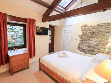 A bedroom with a bed folded towels wooden furniture a window with red curtains and exposed stone wall at Old Coach House Ambleside