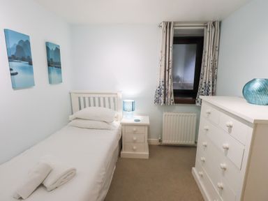 A bedroom with a single bed bedside table lamp dresser and window at Old Coach House in Ambleside
