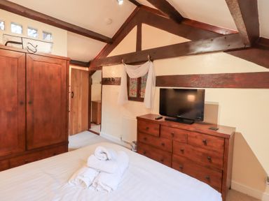 A bedroom with wooden wardrobe and dresser with a television and folded towels on the bed at Old Coach House in Ambleside