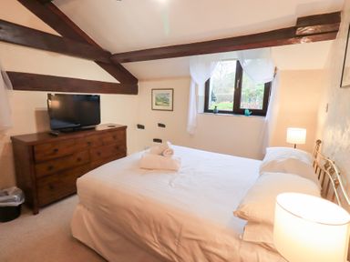 A bedroom with a bed white linens wooden dresser with a television and a window at Old Coach House in Ambleside