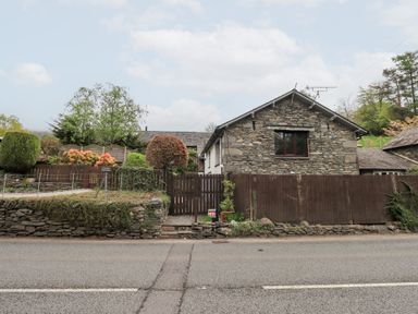 A stone house with a wooden gate and garden behind a stone wall by a road at Old Coach House in Ambleside