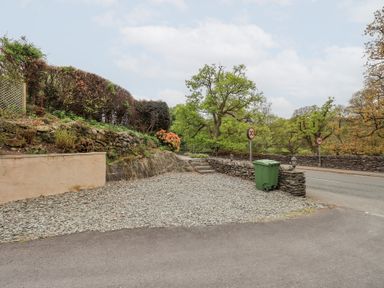 A driveway with gravel and steps leading to a garden area with stone walls and trees at Old Coach House Ambleside