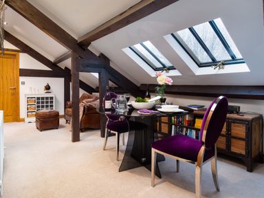 A dining area with a glass table and purple chairs under skylight windows in a room with exposed beams at Hayloft in Windermere