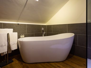 A bathroom with a freestanding bathtub towels on a stand and dark wall tiles at Hayloft in Windermere