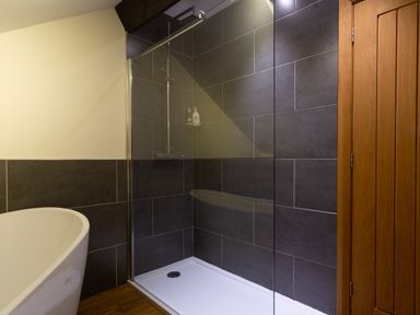 A bathroom with a shower enclosure with dark tiles a freestanding bathtub and a wooden door at Hayloft in Windermere