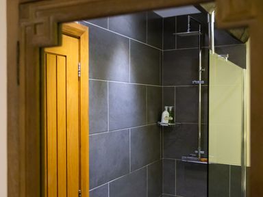 A shower area with dark grey tiles and a wooden door at Hayloft in Windermere