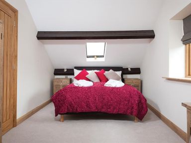 A bedroom with a bed with red bedding and pillows under a skylight at Hayloft in Windermere
