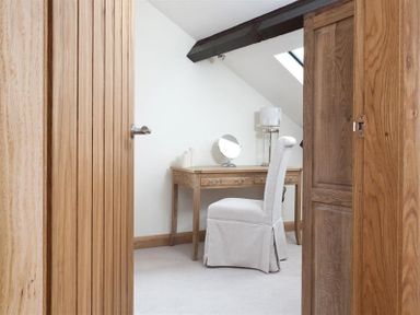 A small room with a wooden desk a chair a lamp and a mirror at Hayloft in Windermere