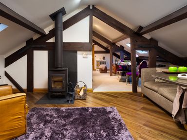 A loft living area with wood beams a wood stove purple chairs and a dining table at Hayloft in Windermere