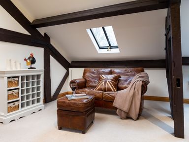 A living area with a brown leather sofa and matching ottoman under a skylight at Hayloft in Windermere