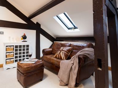 An attic living area with a brown leather sofa and ottoman a white storage unit with baskets and a skylight window at Hayloft in Windermere