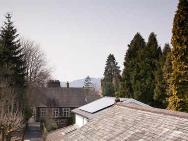 A view of house rooftops and tall trees with a mountain in the background at Hayloft in Windermere