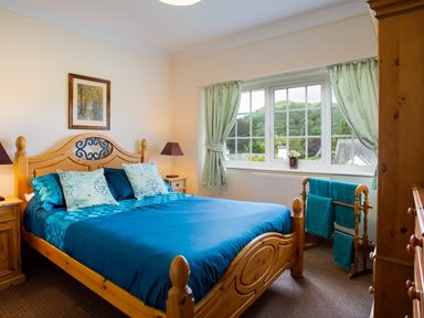 A bedroom with a wooden bed and blue bedding a window with curtains and a wooden towel rack at Uldale in Ambleside