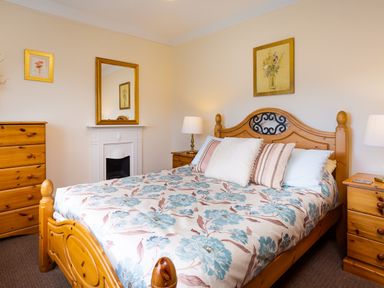 A bedroom with a wooden bed and floral bedspread a wooden dresser a mirror above a fireplace and table lamps at Uldale Ambleside