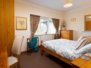 A bedroom with a wooden bed and chest of drawers next to a window with curtains at Uldale in Ambleside