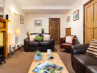 A living room with brown leather sofas a wooden coffee table with magazines a lamp and framed pictures on the walls at Uldale in Ambleside