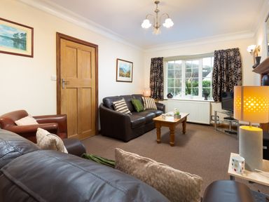 A living room with brown leather sofas a wooden coffee table a window with curtains and a television at Uldale in Ambleside