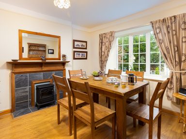 A dining room with wooden table and chairs a window with curtains and a fireplace at Uldale in Ambleside