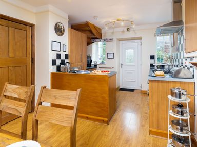 A kitchen with wooden cabinets and chairs a white door and a small rack of pots at Uldale in Ambleside