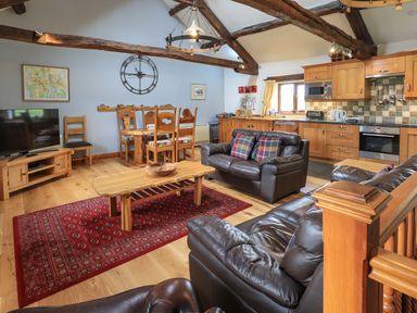 An open plan living room and kitchen with wooden furniture leather sofas and a red rug at Tullythwaite Garth in Crosthwaite